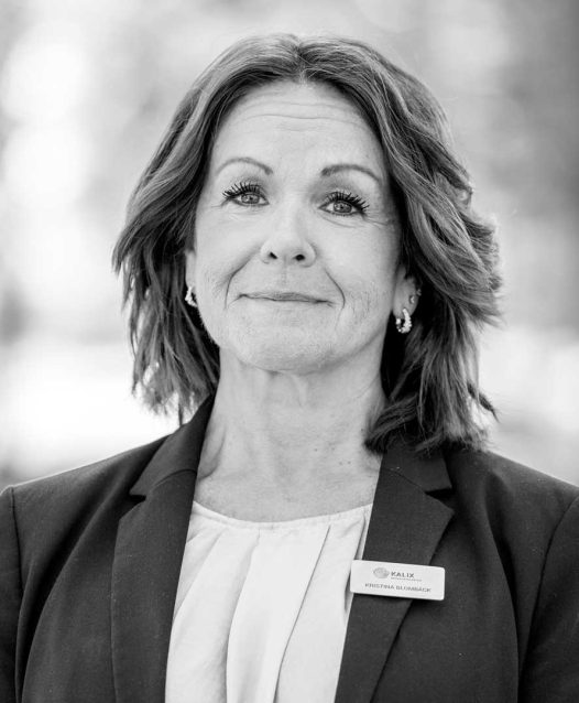 A woman with shoulder-length hair wearing a blazer and name tag stands outdoors, looking forward with a neutral expression. The name tag reads "Kalix, Kristina Blomqvist."