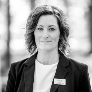 A woman with shoulder-length hair smiles slightly, wearing a blazer and a name tag that reads "KALIX Ulrika Jacobsson Olsson," set against a blurred outdoor background.