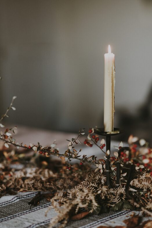Ett tänt ljus på en ljusstake omgiven av torkade blommor.