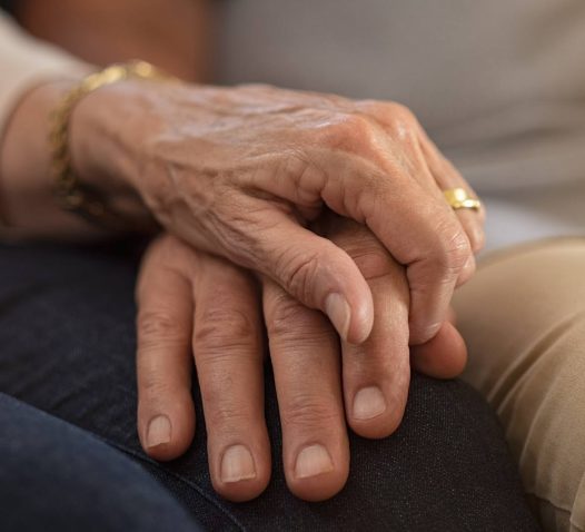 Två händer håller varandra ömt, den ena handen bär en ring.